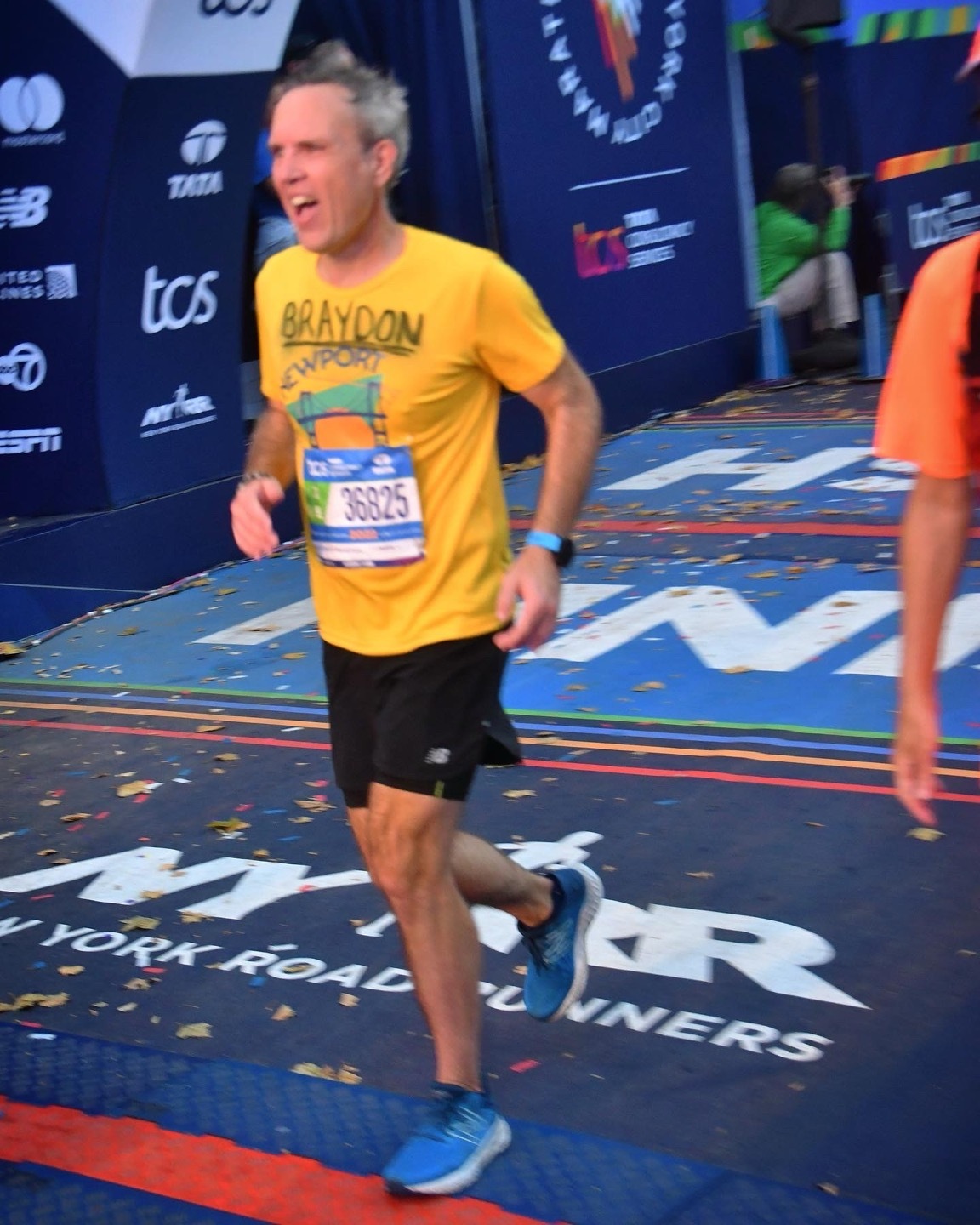 Braydon running through the finish area of the New York City Marathon in a yellow shirt